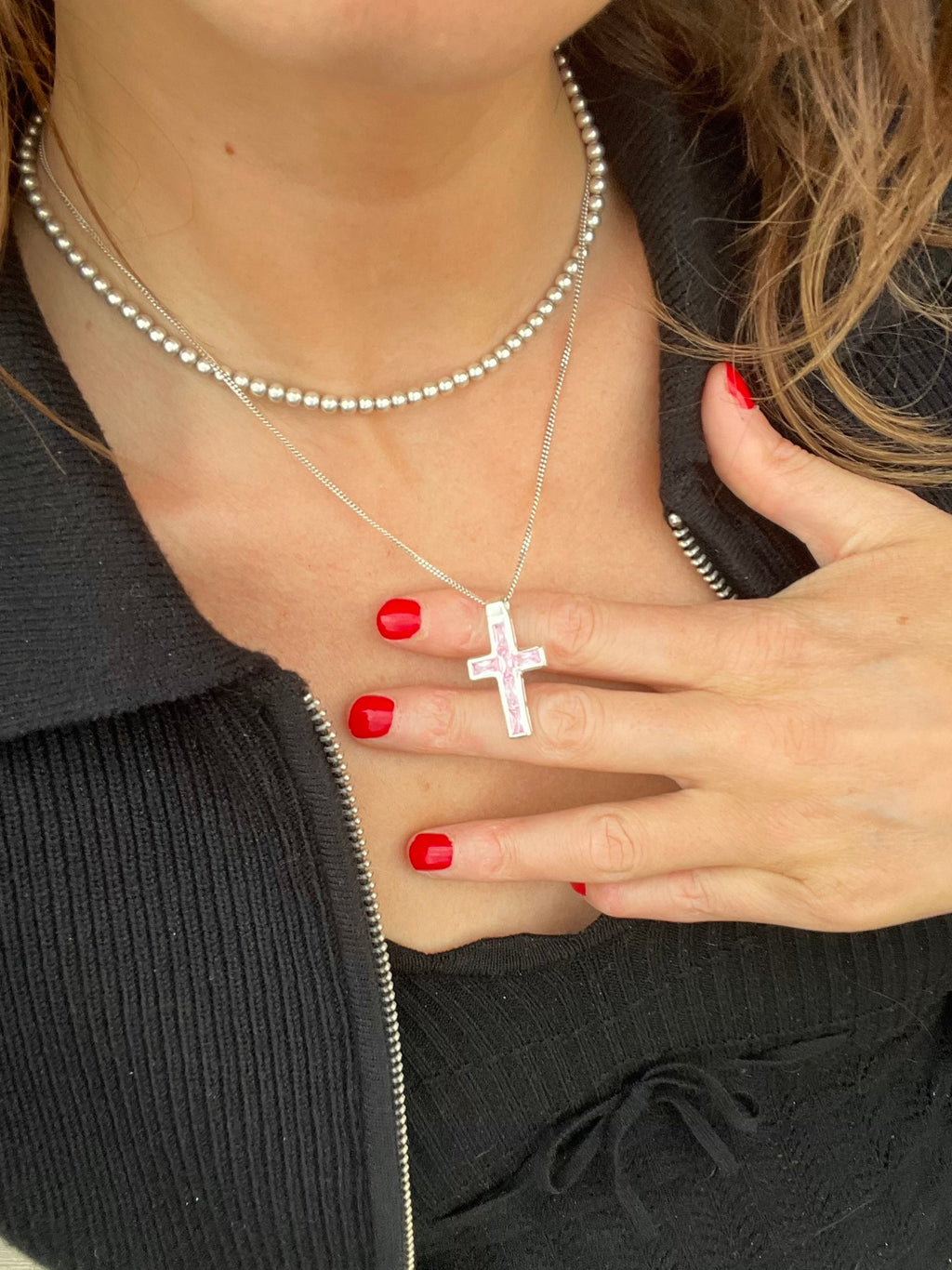 Pink gem cross pendant held between fingers while worn