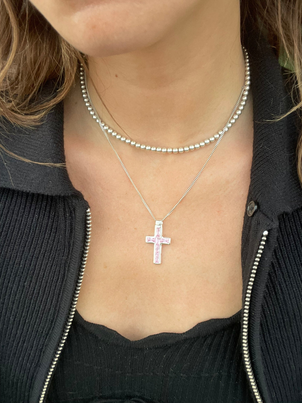 Pink cross necklace worn with a black top, front view