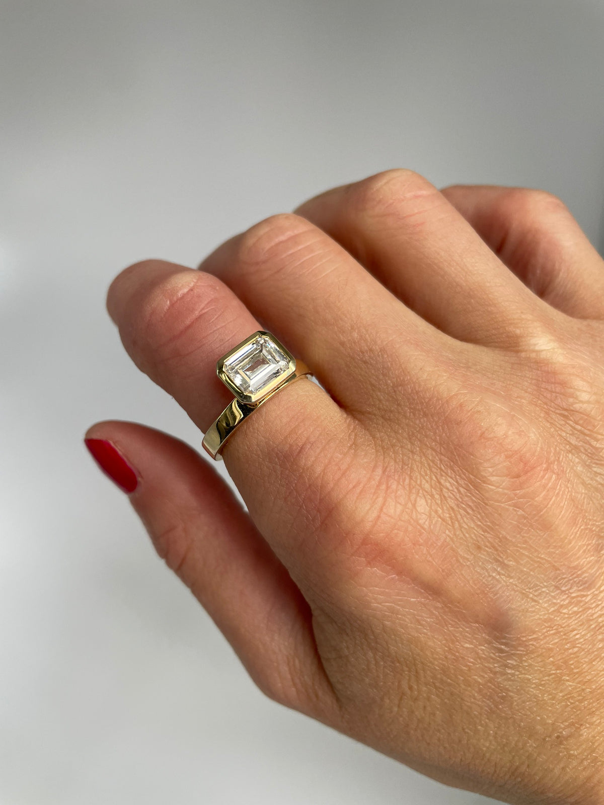 Close view of the bezel set emerald cut stone on the hand