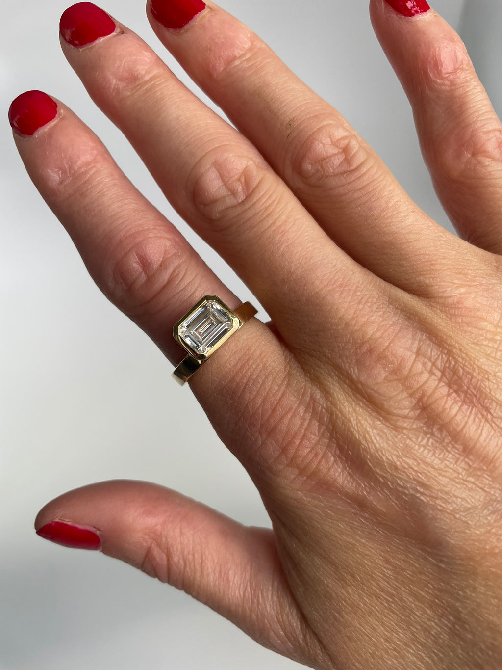 Gold-tone emerald cut ring worn on the hand, angled view