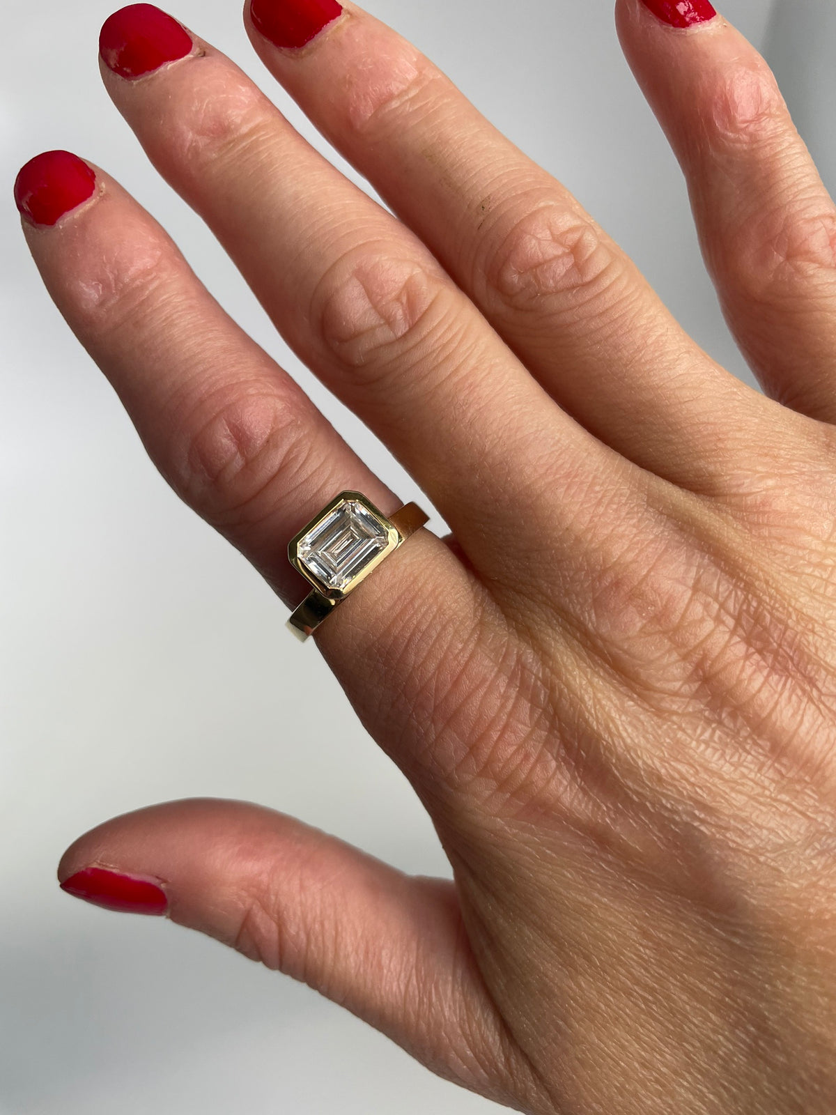 Gold-tone emerald cut ring worn on the hand, angled view