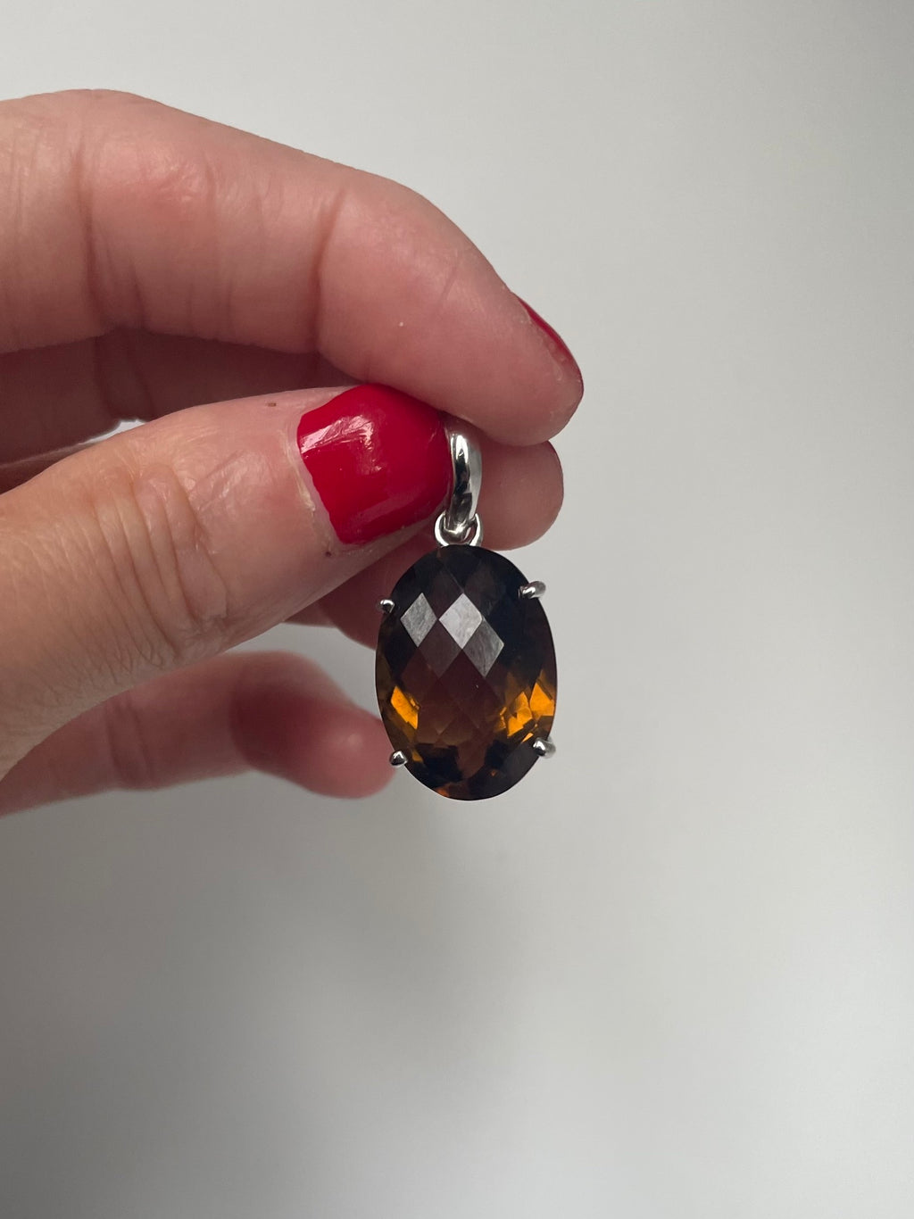 Faceted oval smoky quartz pendant held in the hand, showing the checkerboard facets