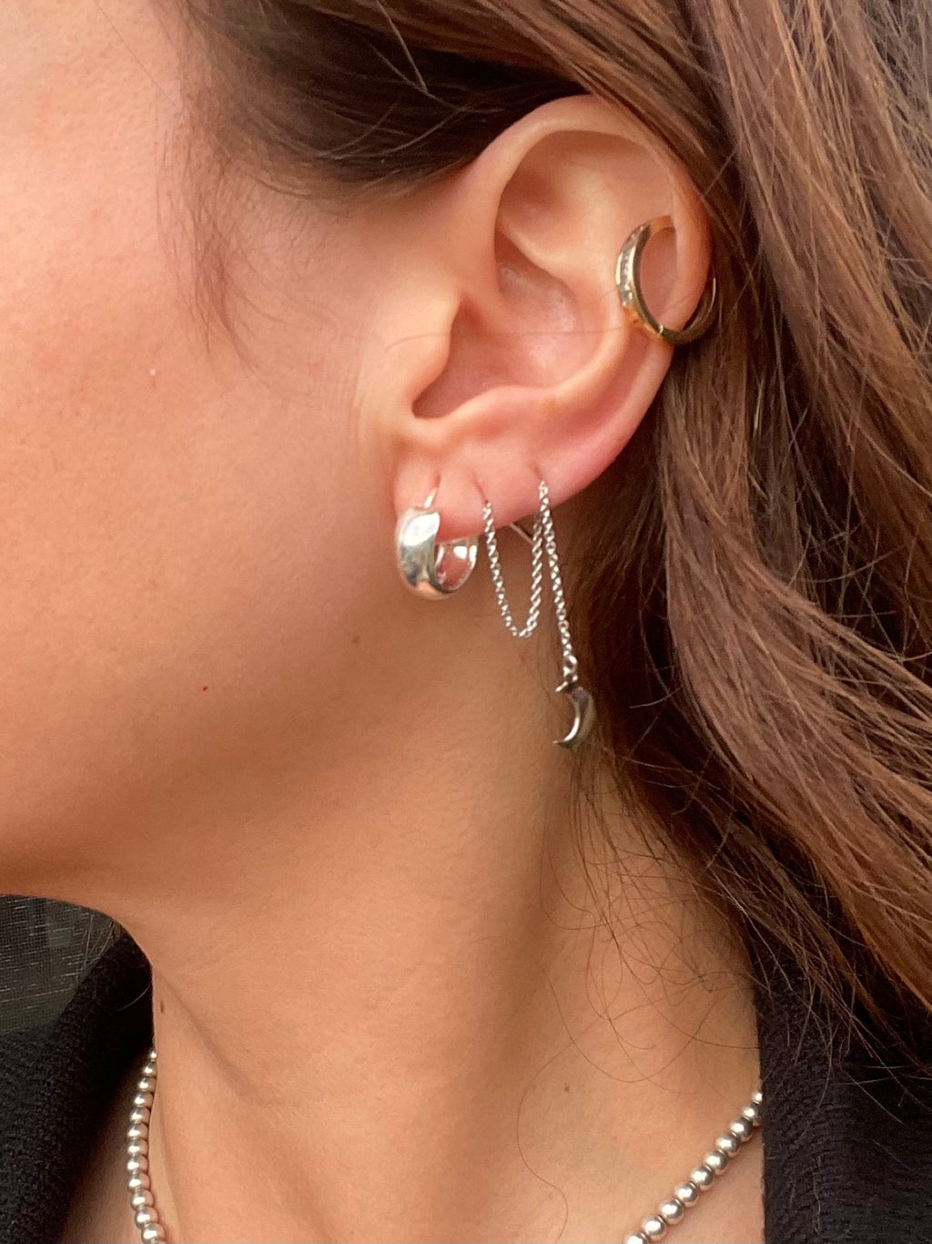 Chunky silver huggie hoop worn on the earlobe, styled with other pieces