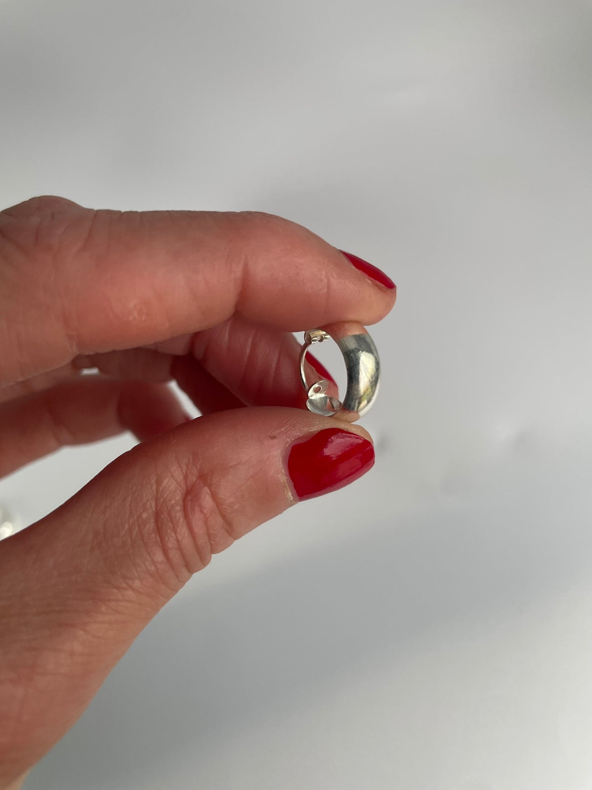 One chunky silver huggie hoop held in the fingers, showing the domed band
