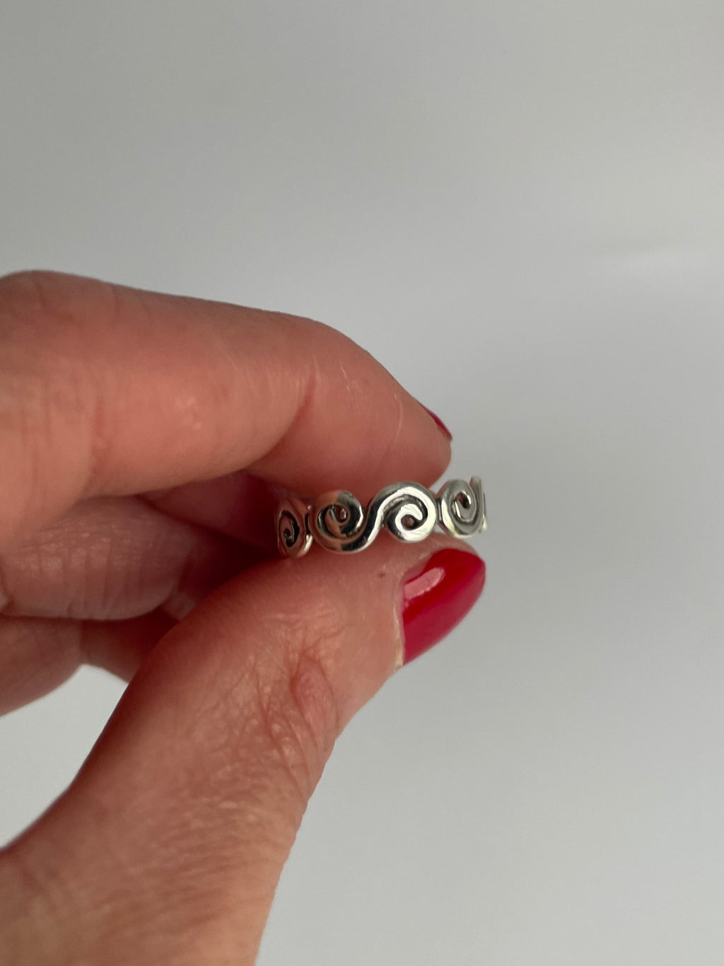 Vintage silver swirl ring held between fingers, showing the openwork spirals