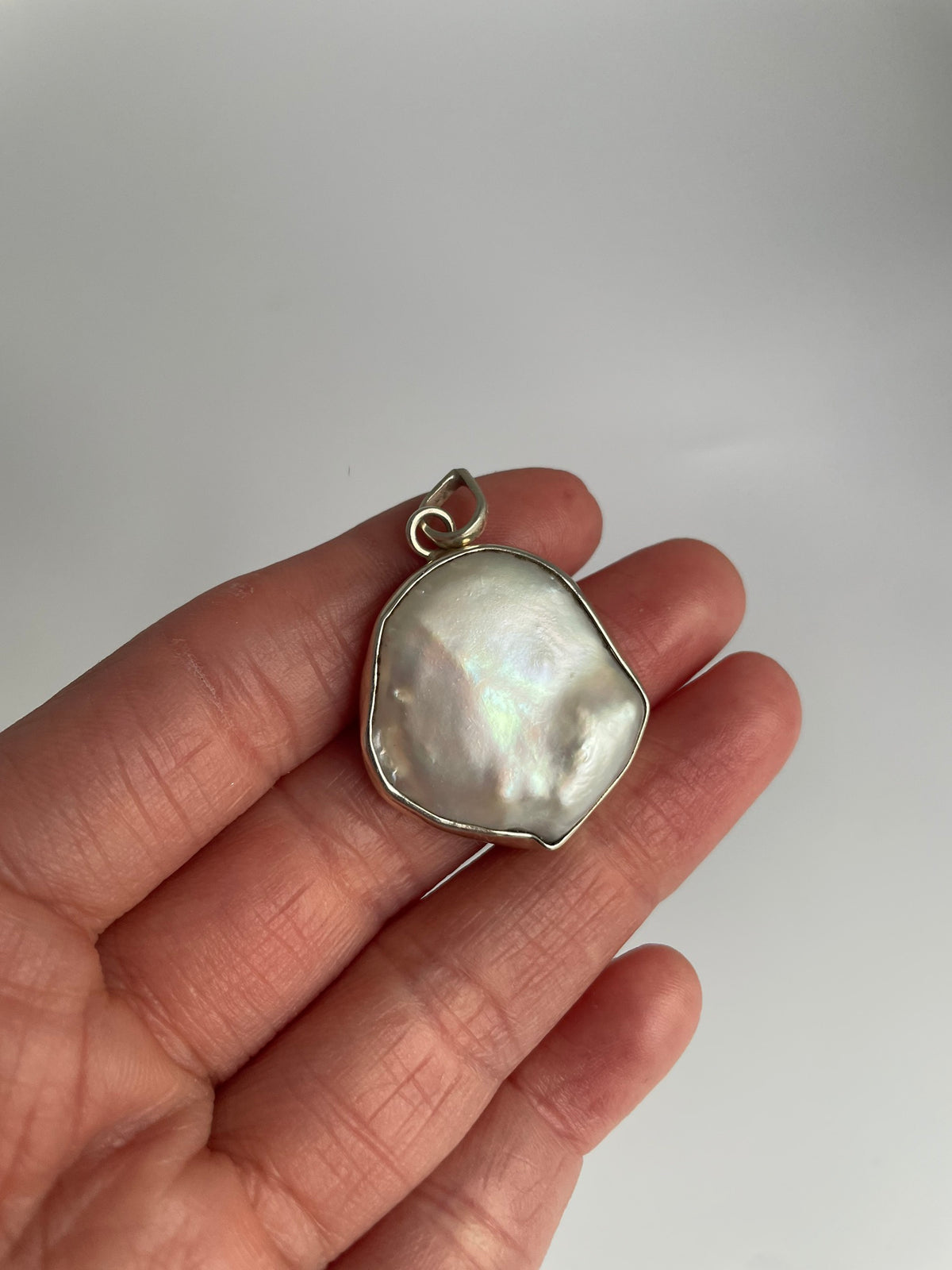 Large freshwater baroque coin pearl pendant in a silver bezel, resting in the palm