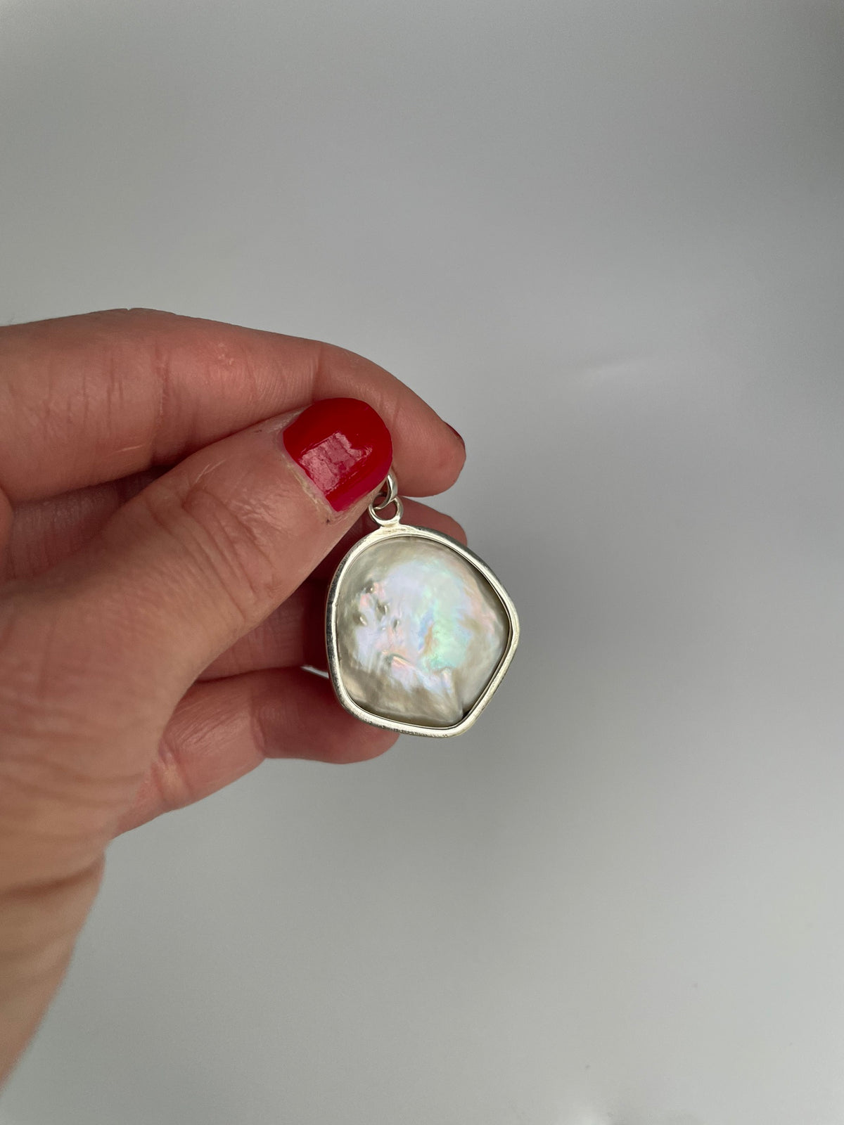 Baroque pearl pendant held between fingers, showing pink and green iridescence