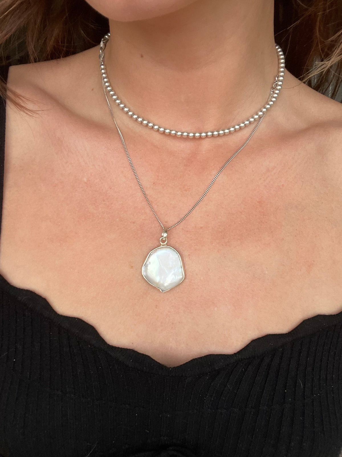 Flat white baroque pearl pendant worn on a chain, styled with a beaded silver choker