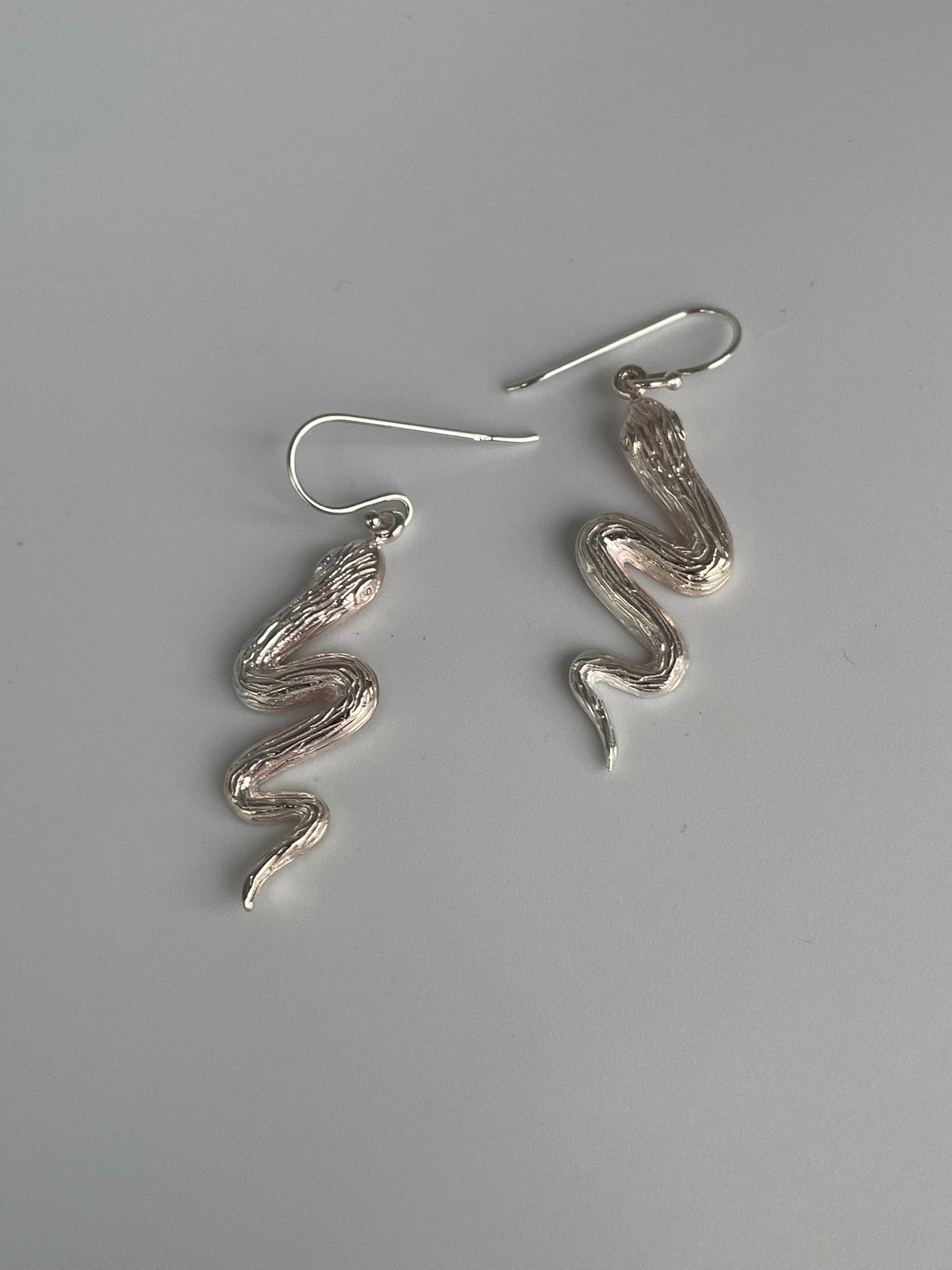 Pair of wavy silver snake dangle earrings with textured scales on fish hook ear wires