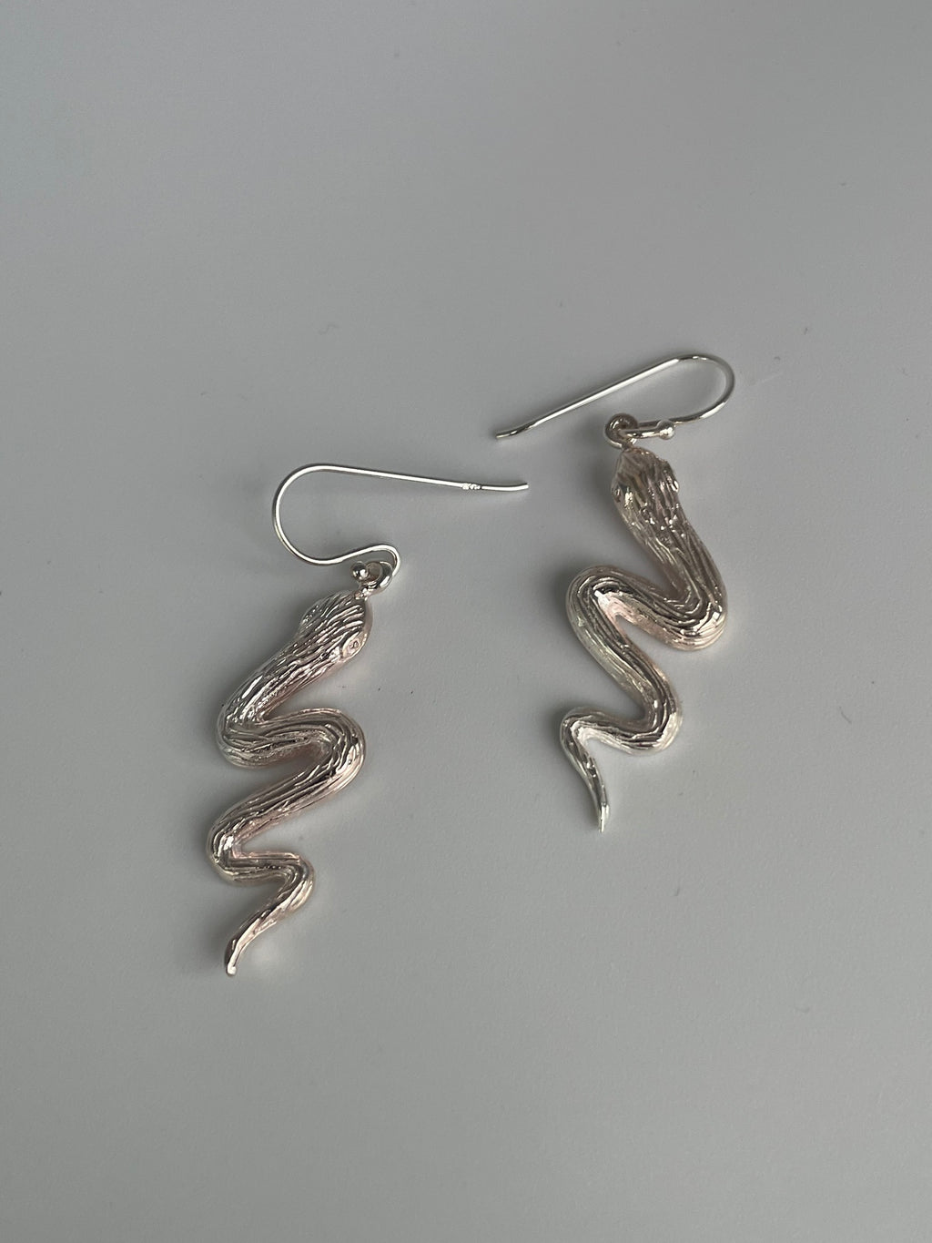 Silver serpent earrings laid flat, showing the S curved bodies and polished highlights