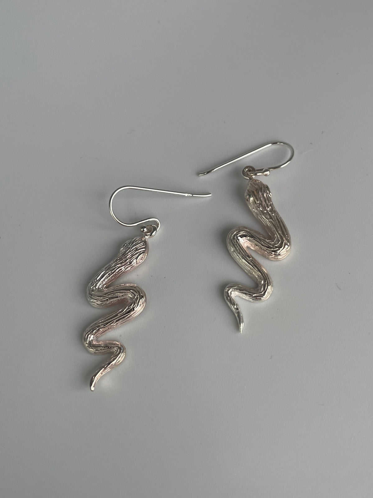 Silver serpent earrings laid flat, showing the S curved bodies and polished highlights
