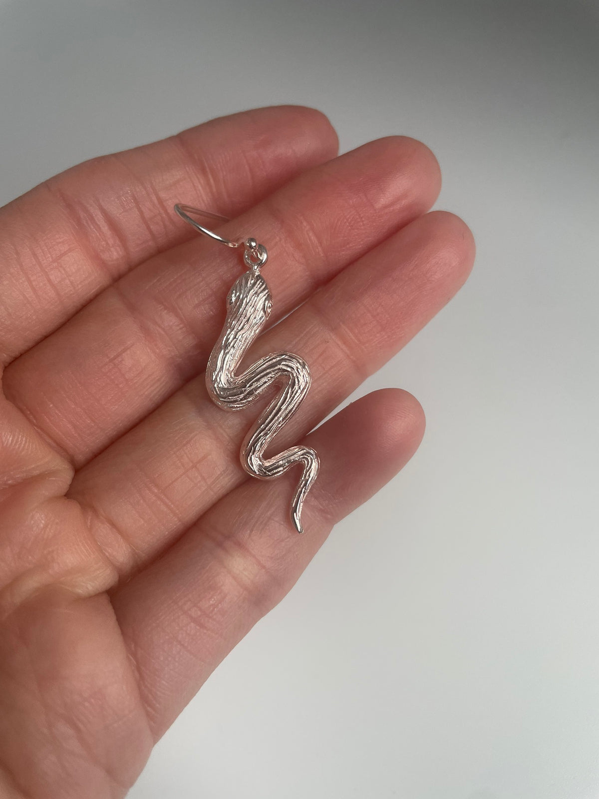 Close up of one silver snake earring on its hook, held in the hand