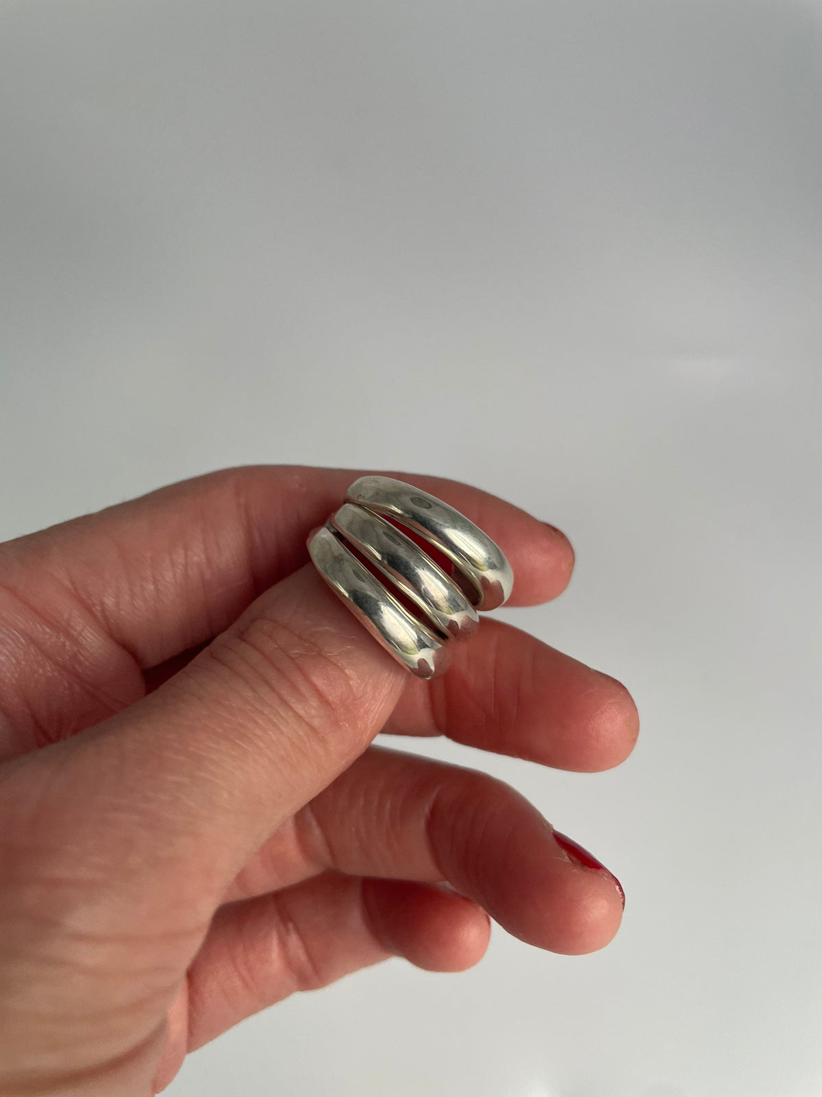Polished silver triple band ring with three domed bands joined at the back, held in fingers