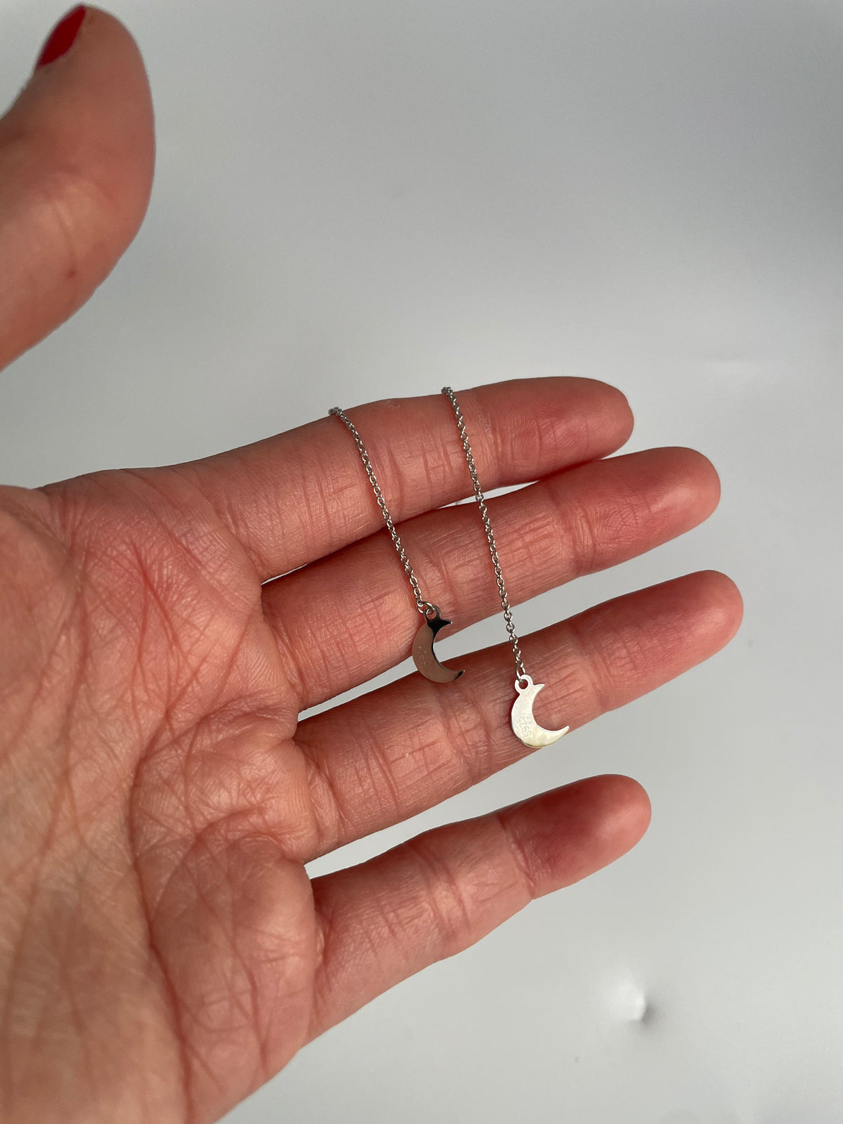 Pair of silver crescent moon threader earrings draped over a hand