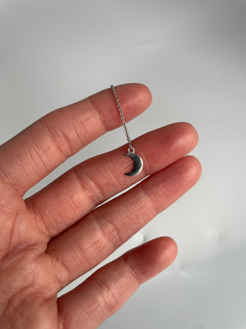 Close up of one flat polished crescent moon charm on a fine chain