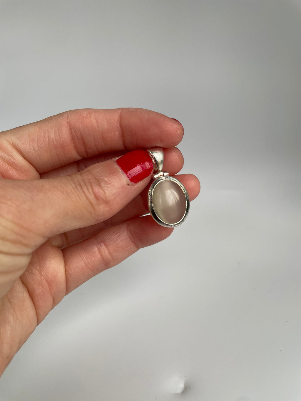 Silver pendant with a milky pinkish white oval cat's eye cabochon, held in fingers