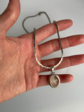 Cat's eye pendant on a flat silver-tone link chain, held on an open hand