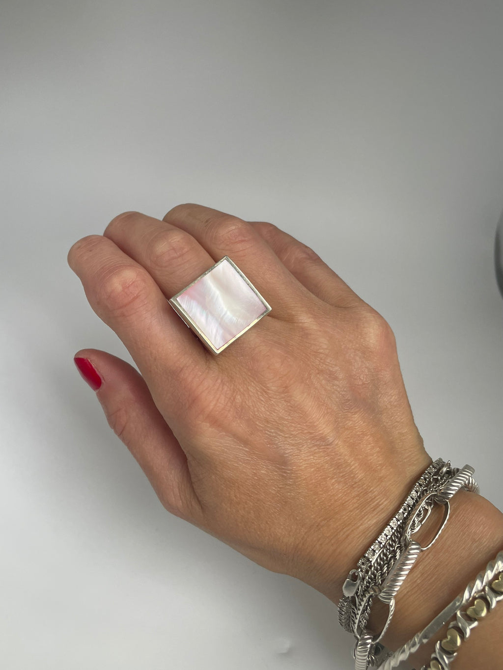 Square mother of pearl statement ring on the hand, with bracelets for styling