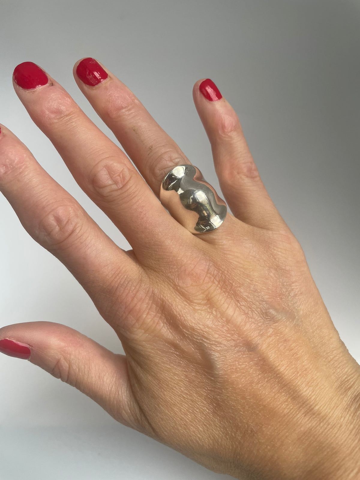Wavy domed silver ring worn on the middle finger, showing its hourglass outline