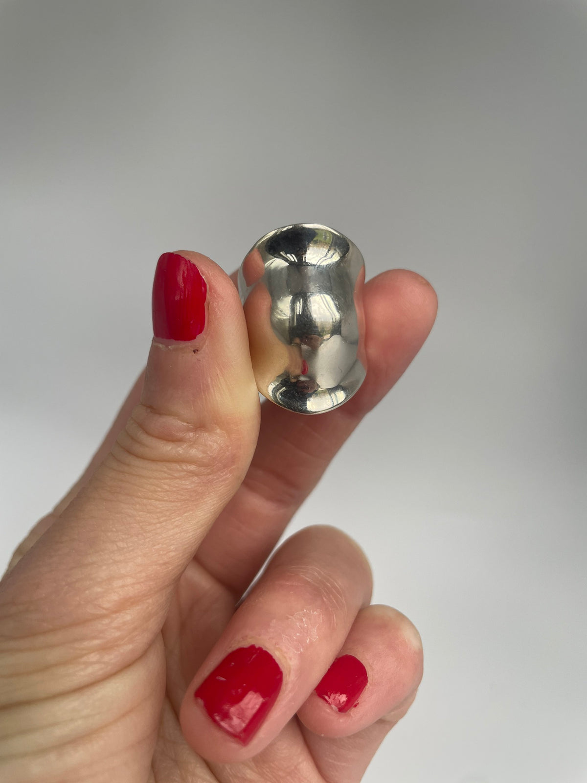 Wide domed silver ring held between fingers, showing the pinched hourglass shape
