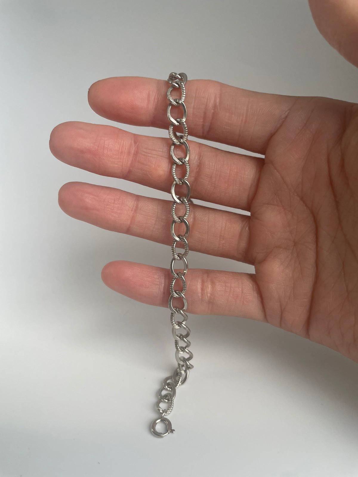 Silver chain bracelet draped over the fingers, showing alternating polished and rope textured links and spring ring clasp