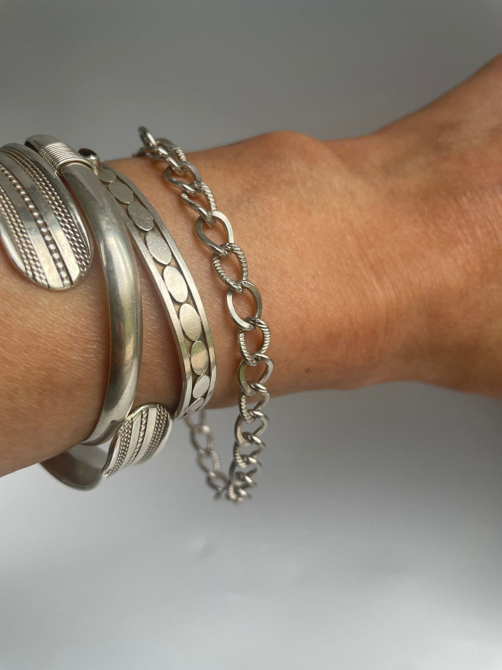 Textured link chain bracelet worn on the wrist, styled with silver bangles