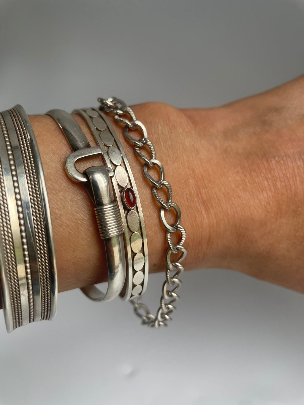 Silver curb chain bracelet worn next to cuffs and bangles for styling