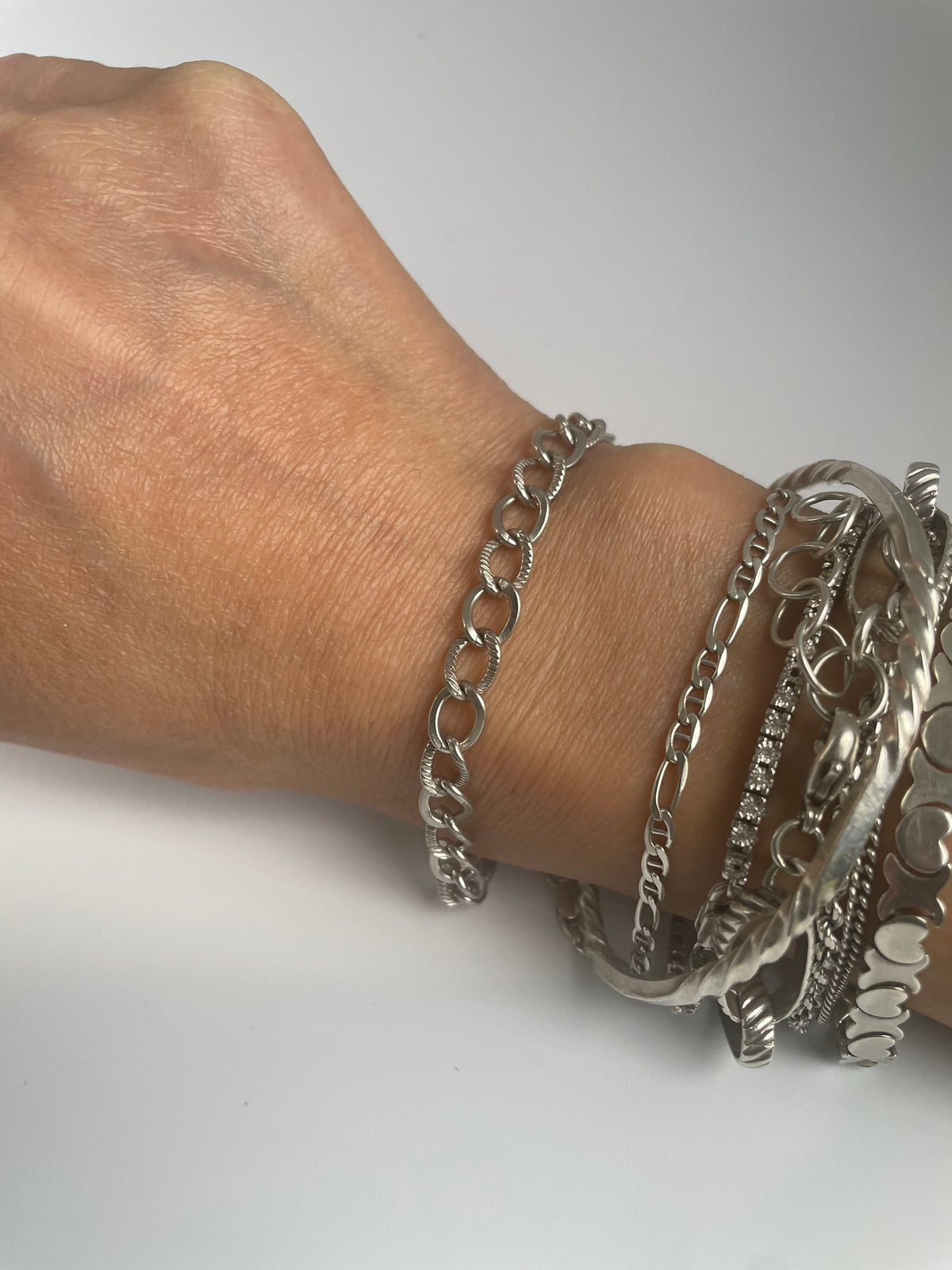 Silver chain bracelet worn on the wrist beside a stack of other bracelets